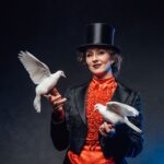 Zauberer Firmenfeier – Frau mit Zylinder in Showkostüm hält zwei weiße Tauben in den Händen